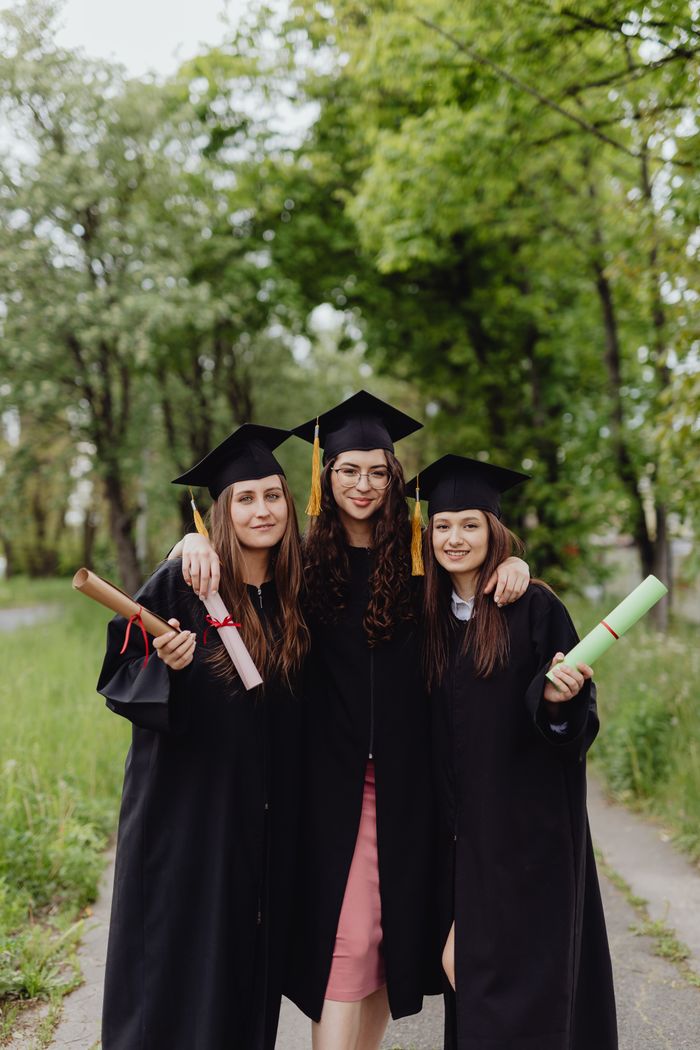 Three young women in graduation gowns celebrating together outdoors.